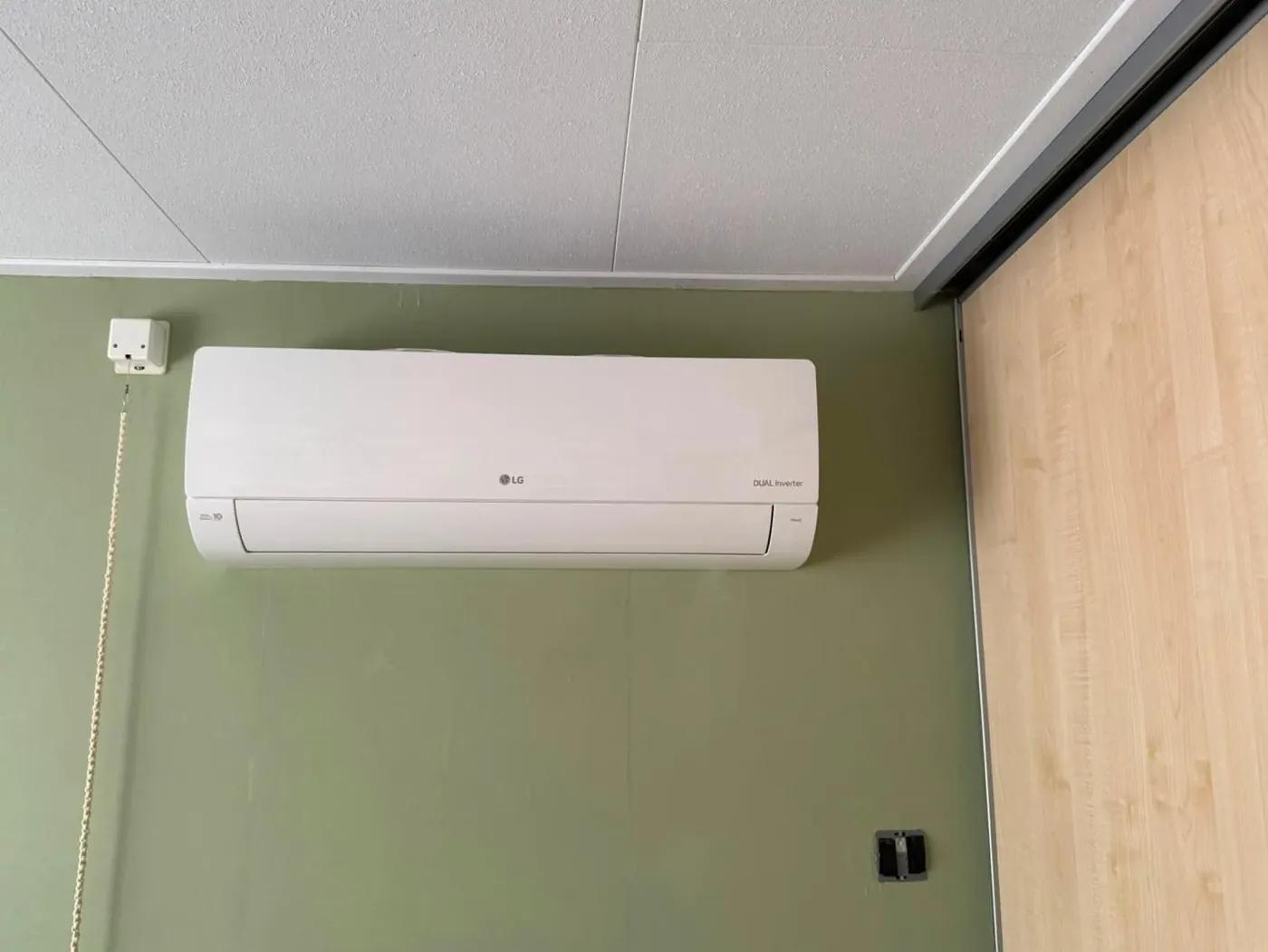 Wit wandmodel airco boven een raam in een woonkamer met groene wand